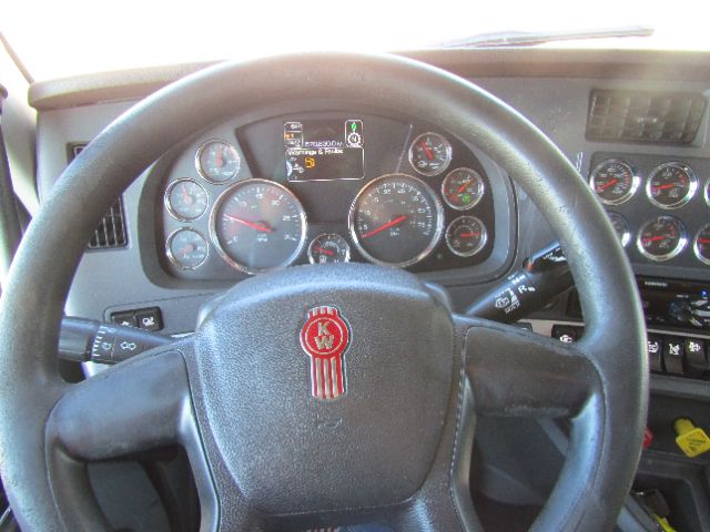 Dashboard view of a Kenworth T680 cab showing multiple gauges and a steering wheel with Kenworth emblem. Center display screens show some icons.