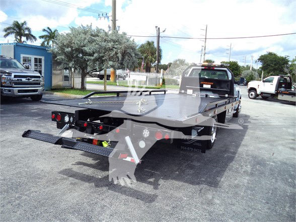 Flatbed tow truck rear view with lowered ramps and hydraulic system on a Chevrolet Silverado 6500HD chassis.