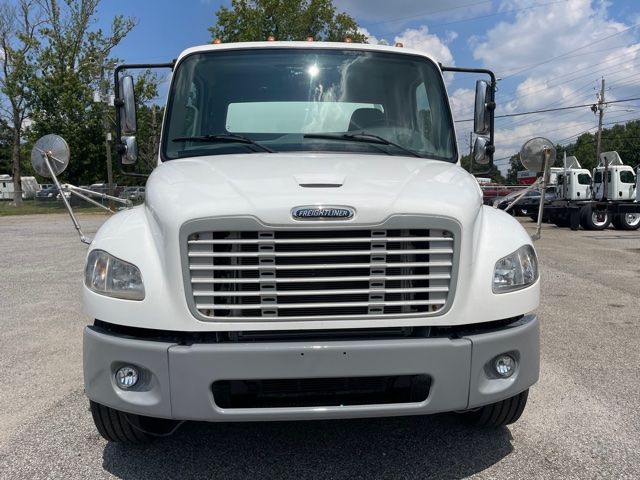 Front view of a white 2013 Freightliner M2 truck with large grille, rectangular headlights, and gray front bumper; side mirrors and clear windshield visible.