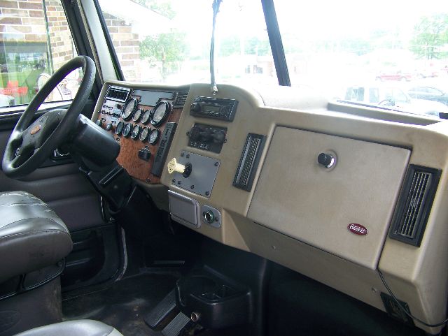 Peterbilt 335 interior dashboard view showing steering wheel, gauge cluster, wood panel, and beige glove compartment.