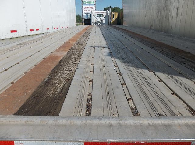 Flatbed trailer interior showing wooden and metal decking with center rails and outer side panels.