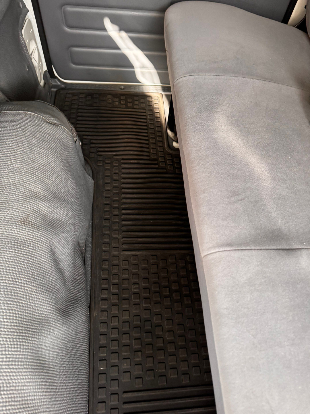 Interior image showing rear passenger area of a 2022 Isuzu NQR with a black ribbed rubber floor mat and gray upholstery.