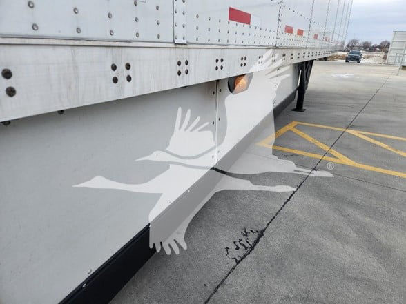 Trailer side view showing lower side panel and silvery exterior with reflective birds graphic and parking lot markings.