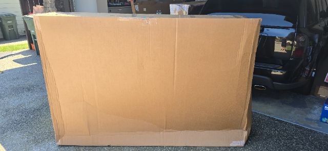 Large cardboard box in a driveway with a vehicle in the background.