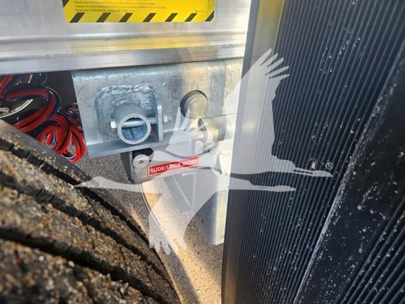Trailer hitch area with electrical cables and a small label on a Wabash trailer showing a side latch and wiring components.