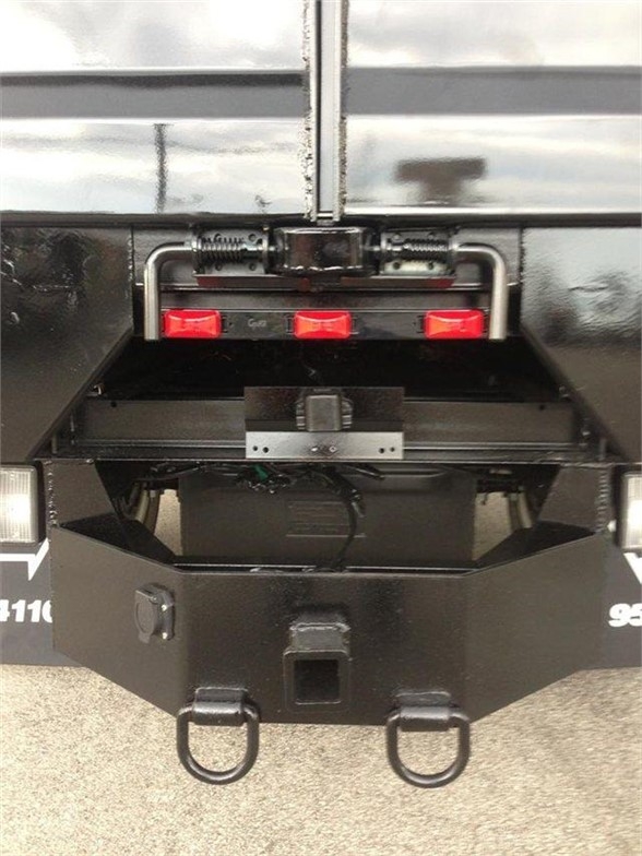 Back of truck showing hydraulic tailgate with two D-ring shackles and hitch receiver, red taillight reflectors, and bumper steps.