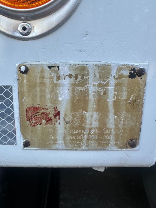 Back of Sterling L8500 vacuum truck showing a weathered nameplate with illegible text, one red emblem area, and a small vent/grille to the left.