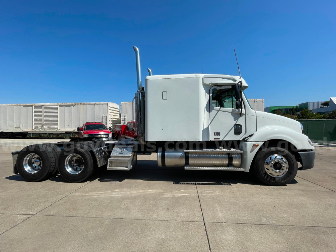 Truck cab and chassis showing side profile of a white Freightliner Columbia 120 with chrome fuel tanks and dual rear axles.