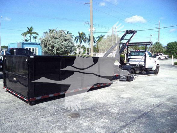 Flatbed truck with a large black dump-like trailer in a parking lot; Chevrolet Silverado 6500HD image with a white truck in background.