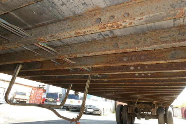 Great Dane trailer undercarriage showing rusted I-beam cross members and leaf spring suspension with wheels at rear.