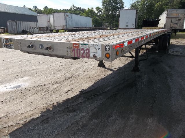 Flatbed trailer showing rear deck with attachment points and wheels in the distance; numbered plate 1028 on side.