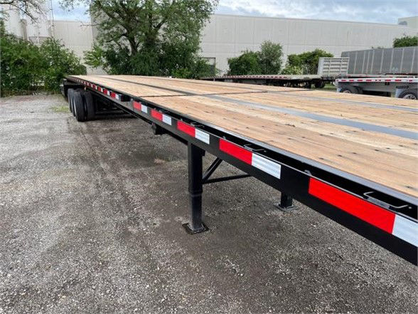 Flatbed trailer deck with wooden planks and black steel frame, side railing with red and white reflective tape.
