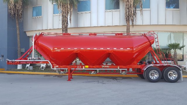 Pneumatic dry bulk trailer in red with multiple compartments and tandem axles.