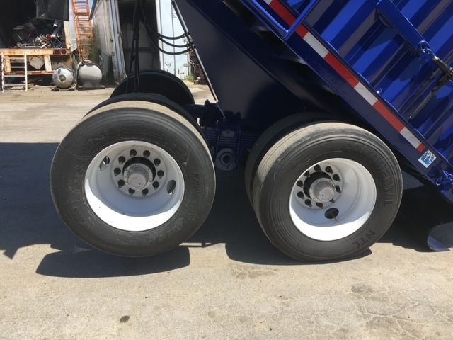 Two rear wheels of a blue utility dump trailer with white rims; part of the dump bed is visible above.