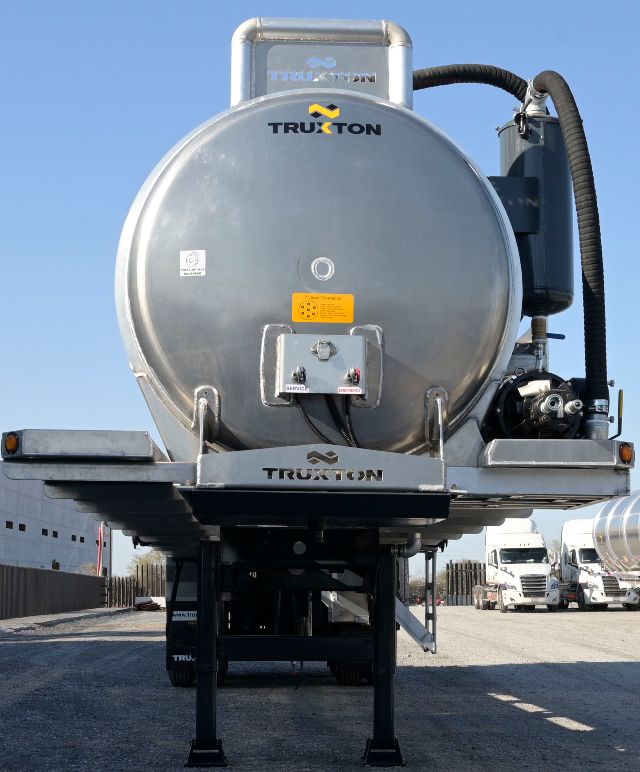 Truxton aluminum vacuum trailer rear view with circular tank and support legs, Truxton branding, and attached piping on right side.