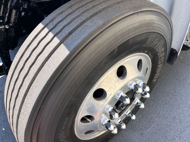 Front wheel of a Freightliner M2 cab and chassis showing tire and polished hub with lug nuts.