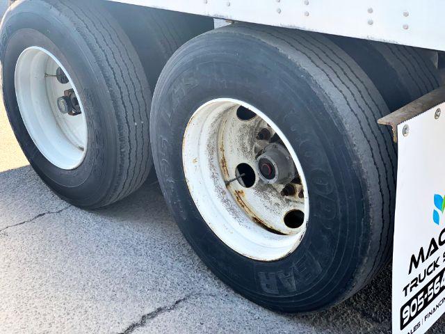 Two wheels of a trailer with white rims and black tires; rusty inner wheel area and part of a white body with a small colored logo. No other text clearly visible.
