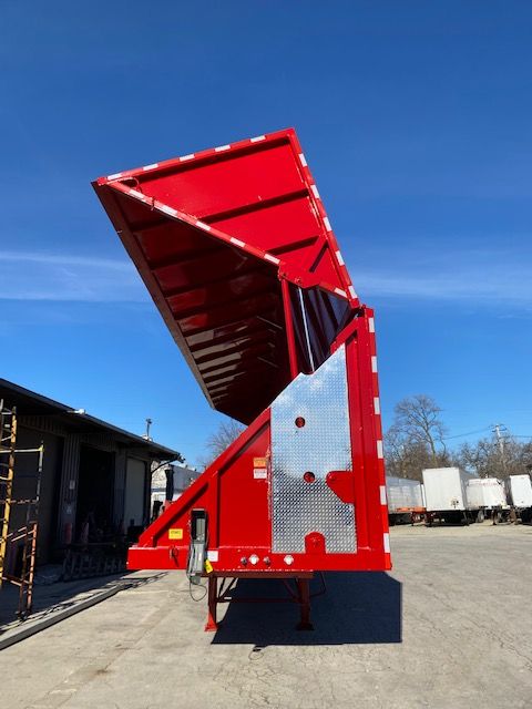 Red Transcraft trailer with a raised rear loading ramp and diamond-plate platform, showing metal edges and support structures.