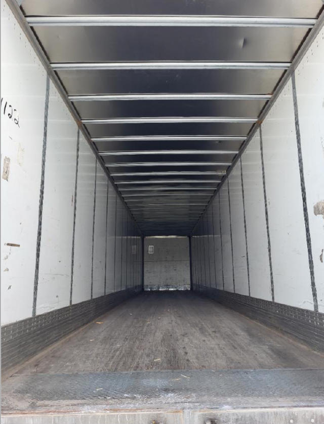 Inside the empty cargo trailer with metal walls and ceiling, wooden floor, long narrow space displaying overhead rails.