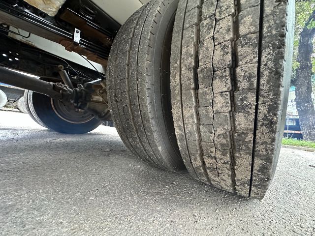 Dual rear axles with worn tread lines on ribbed tires; undercarriage components and suspension visible near wheel wells.