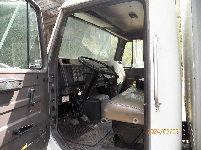 Truck cab interior of a 1993 IC Corporation 4700 showing steering wheel, dashboard, bench seat, and entry door. Date stamp 2024/03/03 visible.