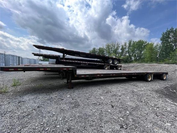 Dynaweld steel stepdeck trailer with stacked drop deck sections on a gravel lot; long flatbed with two rear axles and a set of metal steps/steps on top.