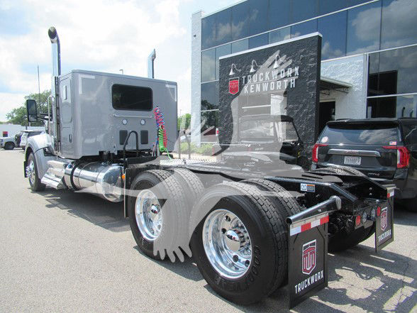 Kenworth W990 tractor in showroom with chrome fuel tanks and dual rear axles, showing 6 tires and rear hitch area.