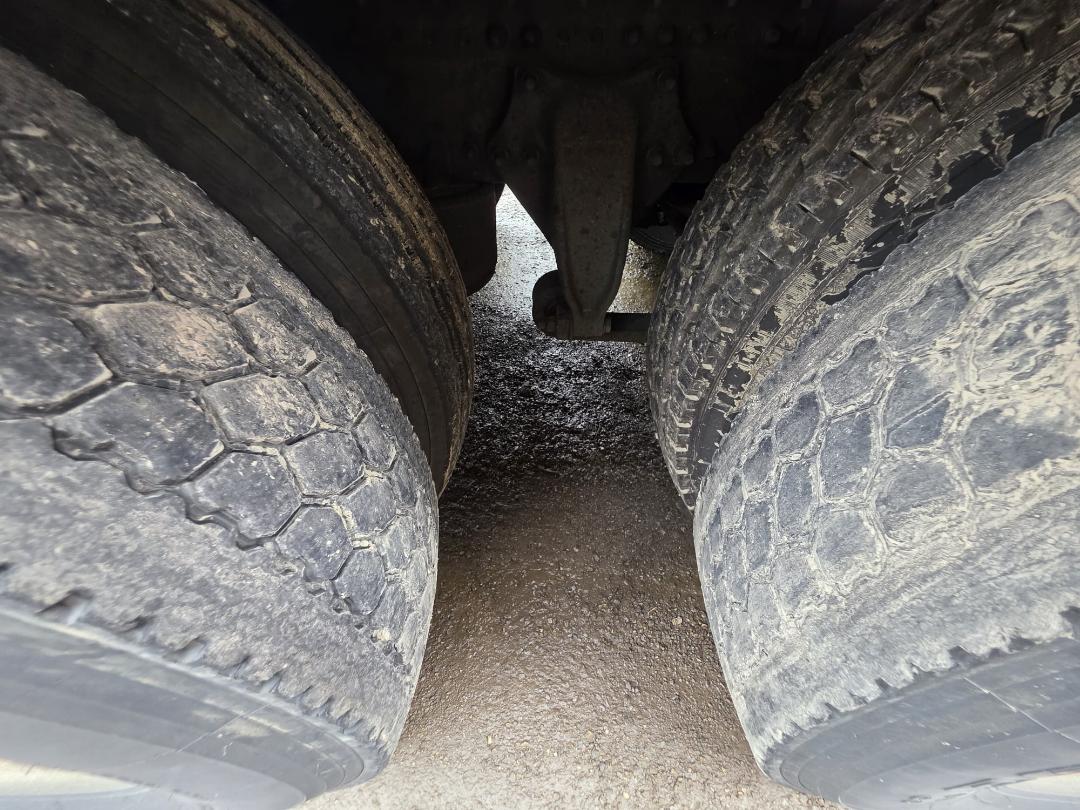 Truck dual rear wheels with heavy tread, view under a Freightliner Cascadia showing tires and suspension components.