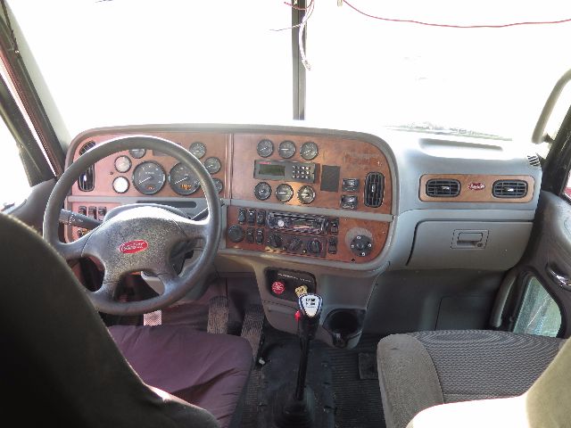 Peterbilt truck interior dashboard with woodgrain panels, steering wheel, gauges, and gear shift visible.