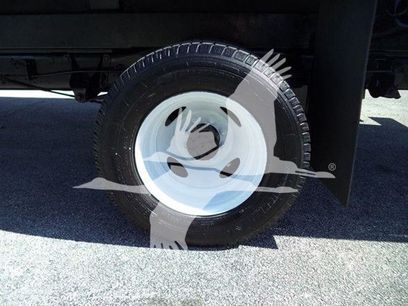Ford E450 wheel with white steel rim and black tire, side view under flatbed.