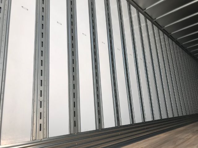 Trailer interior showing vertical white insulated panels and corrugated metal floor, long row of stake pockets along wall.