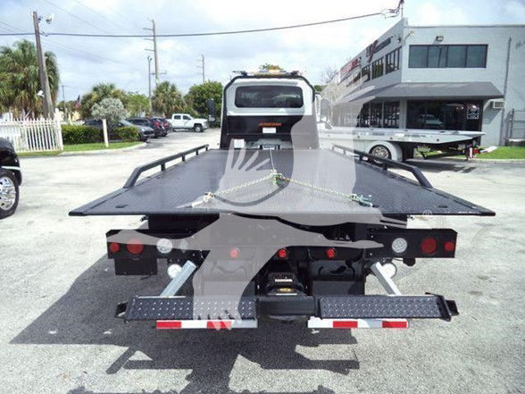 Tow truck with flatbed and rear view of equipment showing loading bed and winch, International MV chassis in background.