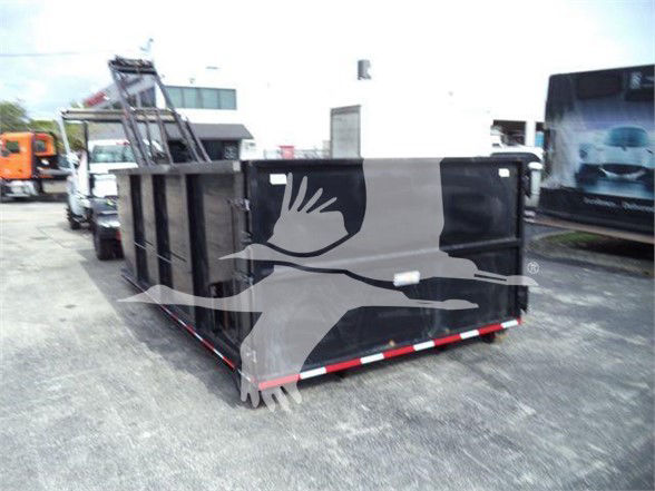 Truck bed or dumpster trailer in a lot; black rectangular container with metal sides and red/white reflective strip on lower rear edge.