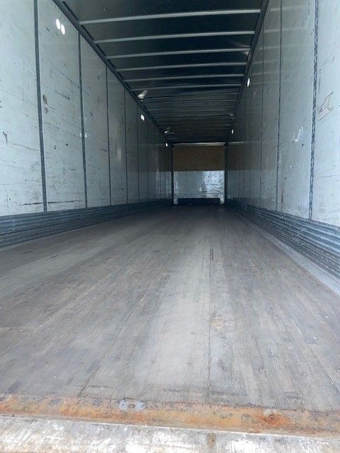 Interior of an empty trailer with wooden floor and metal side walls, long rectangular cargo space, rear opening visible.