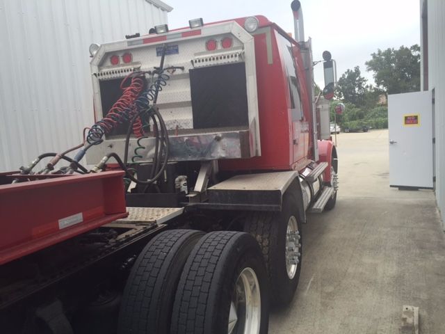 Semi truck (red) rear sleeper cab with dual rear axles and exposed air lines/coiled hoses, chrome steps, and fuel/air connections.