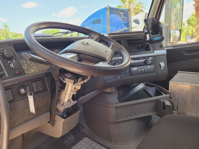Volvo truck dashboard interior showing steering wheel, instrument cluster, center console with controls and a mounted tablet; includes gear selector stalks and dash panels.