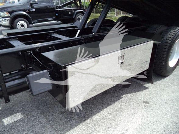Truck chassis with a rectangular rectangular tool storage box mounted beside the rear wheel. Visible text on labels/button not legible.