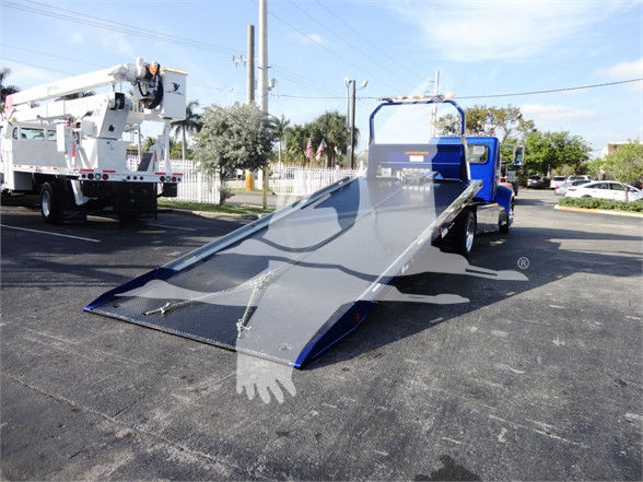 Tow truck with a blue cab and a long metal rear ramp, flatbed tilt surface, parked in a lot.