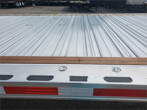 Flatbed trailer deck with aluminum surface and rear bumper, showing riveted corrugated metal and rear taillight area.