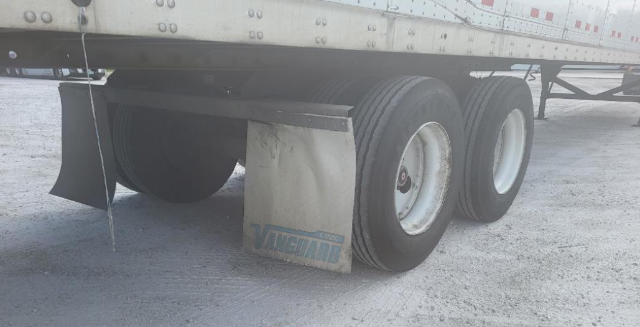 Rear dual-tire trailer axle showing mudflap with blue text, and wheel rims; part of a Vanguard trailer with chrome sides.