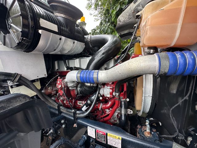 Engine bay of a 2017 Mack GU713 vacuum truck showing red engine, hoses with blue clamps, black intake, and orange coolant reservoir.