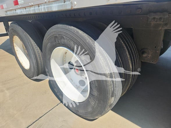 Dual-axle trailer with Goodyear tires, white rims, undercarriage and frame visible; tires show tread and wheel covers.