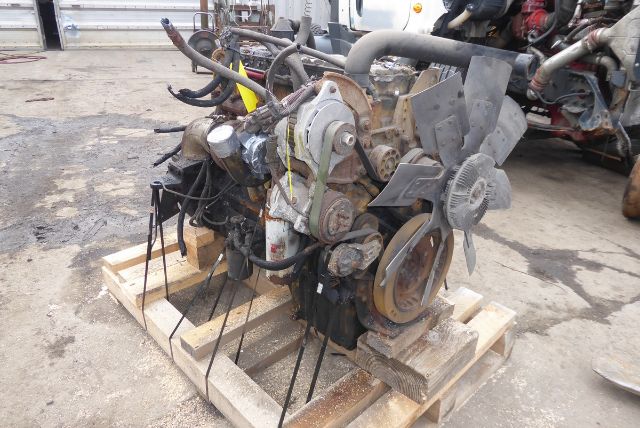 Truck engine on a wooden pallet with belts, pulleys, and cooling fan assemblies visible.