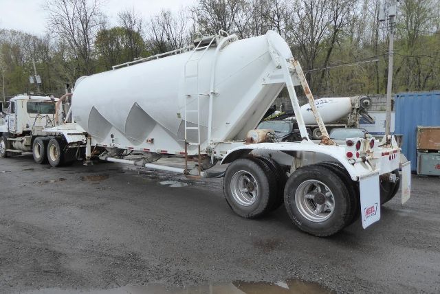 Fruehauf dry bulk trailer in side view showing cylindrical tank and dual rear axles with white paint.