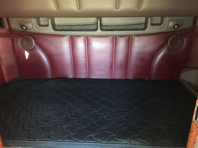 Peterbilt truck interior showing maroon leather seats and backrest with storage area and quilted headliner visible.
