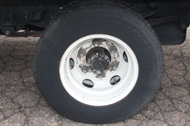 Isuzu NPR-HD truck wheel with white steel rim and lug nuts; visible tire tread and road surface.