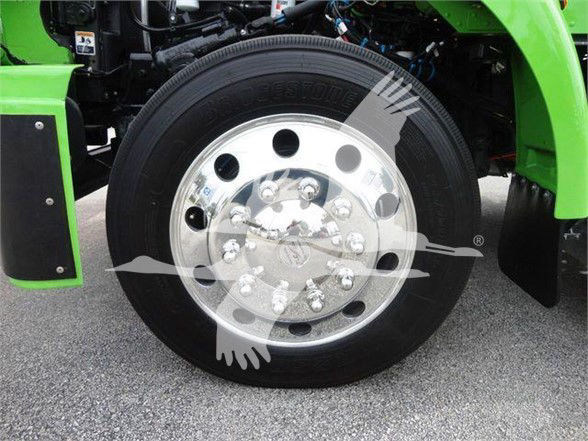 [Wheel] Front wheel of a 2022 Peterbilt 337 with chrome hub, black tire, green fender, and towing equipment visible.
