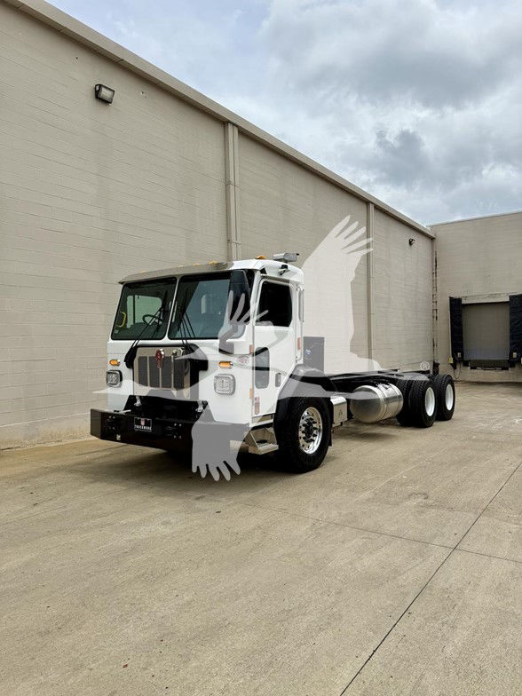 Kenworth L770 cab and chassis truck in white with front grille and dual rear axles, side fuel tank, parking lot setting.