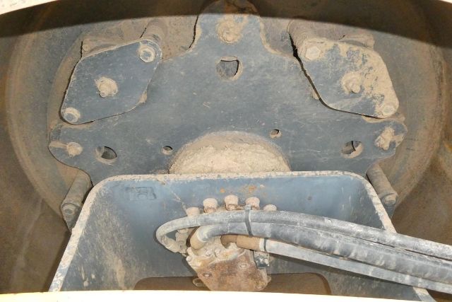 Trucking equipment axle and hydraulic hoses on Vibromax VM106D undercarriage with blue metal frame and dusty surfaces.
