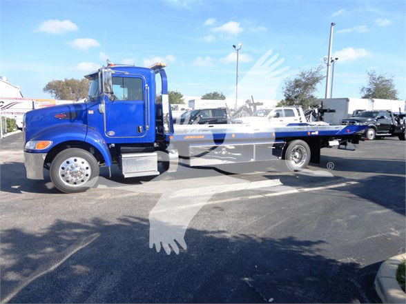 Blue 2022 Peterbilt 337 tow truck on lot with flatbed, side view showing cab and long bed.
